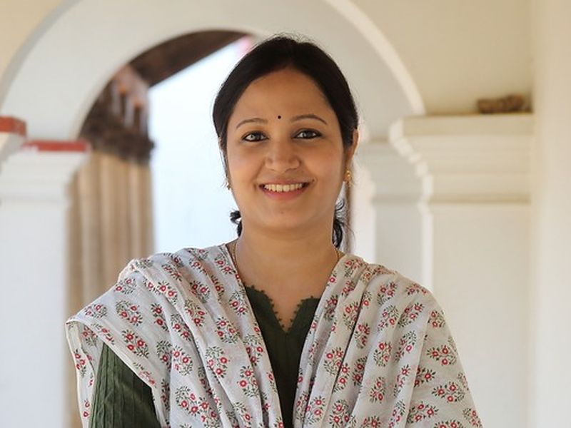 A smiling woman in a printed shawl standing in a colonnade.